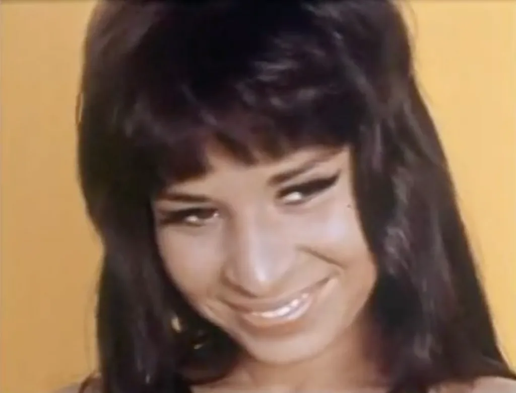 Palva Itano in the film 'Wild Gals of the Naked West' she is smiling brightly against a yellow background.
