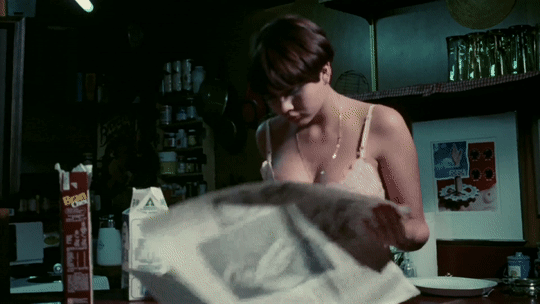 Desiree Cousteau sits on a chair, casually reading a newspaper, captured in a relaxed and natural moment.